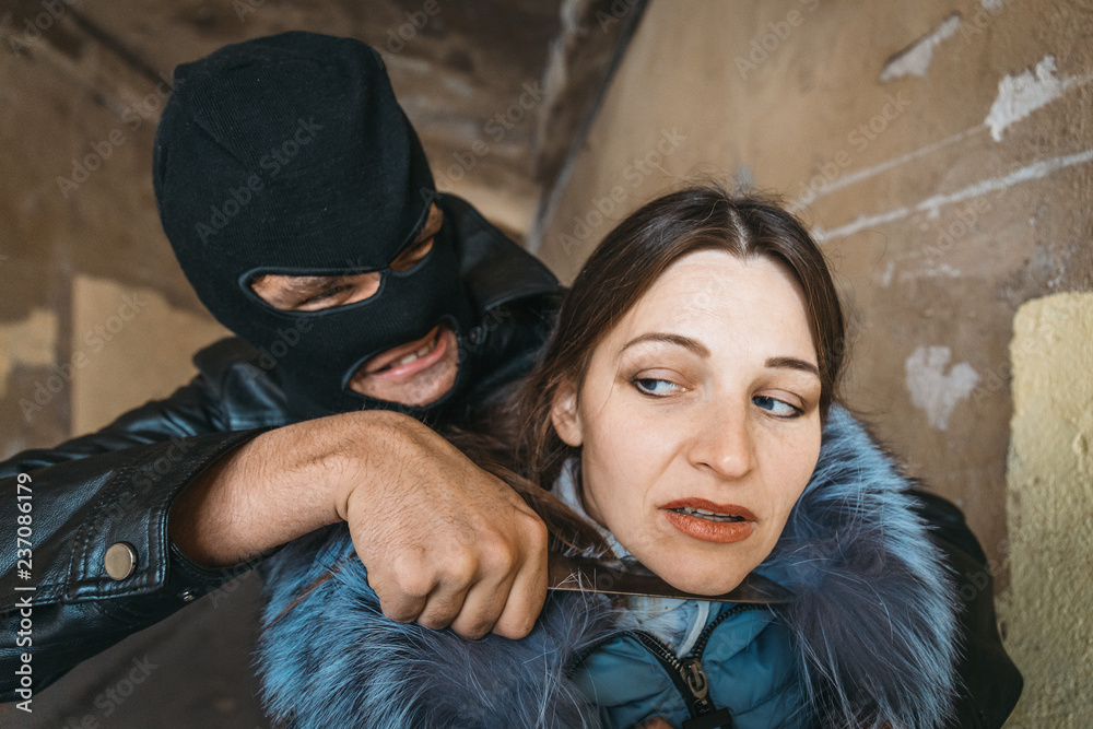 Masked robber man put knife to female victim's throat Stock Photo