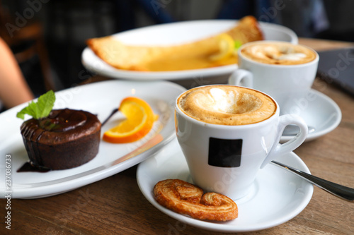 Two afternoon cups of beautifully arranged cappuccinos, lava cake and lemon pancake.
