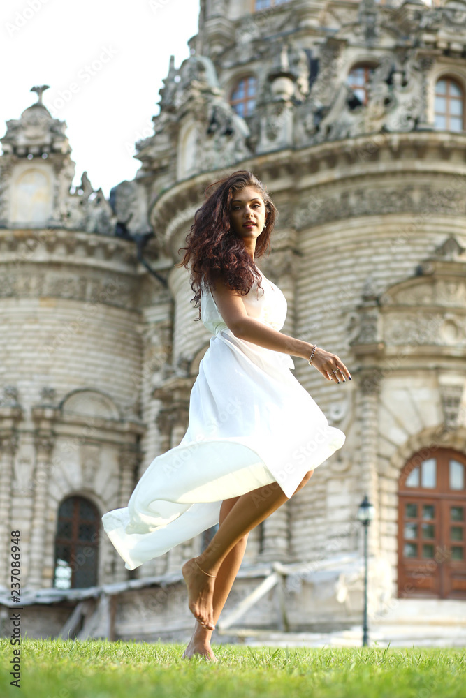 Young beautiful brunette woman in white flowers dress walking on the street Young beautiful brunette woman in white flowers dress walking on the street