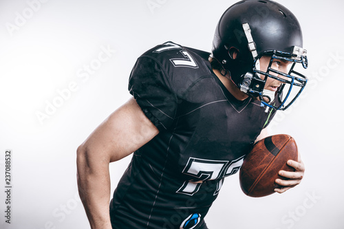 American football player wearing black helmet and jersey serving the ball in motion isolated over white background