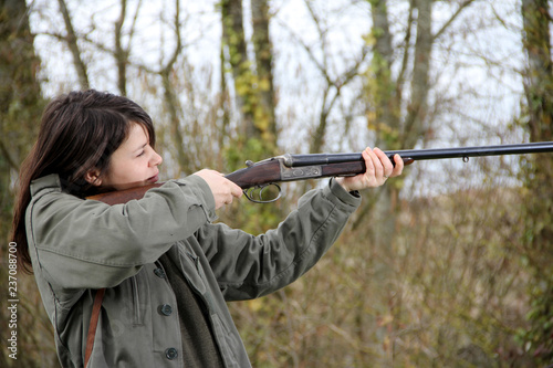 young woman hunter in action, aiming with her vintage shotgun.