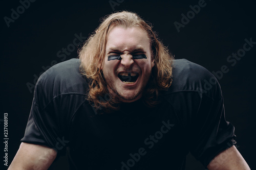 Caucasian football player clenches fists with happiness, being in high spirit, open mouthes with missing tooth widely, have overjoyed expressions, celebrate their winning, pose indoor. photo