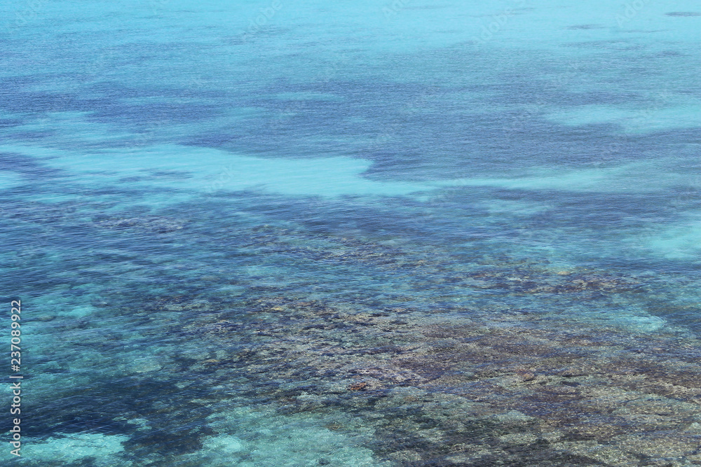Fototapeta premium Looking down at the green, blue, and turquoise waters of the Caribbean Sea, Montego Bay, Jamica. A rocky sea bed can be seen in the shallow area.