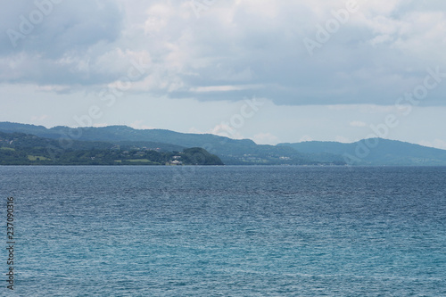 Looking across the water at the green  tree cover  hills beyond  Montego Bay  Jamaica. Water has a slight ripple. Sky is overcast.