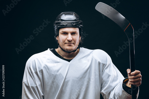 Professional caucasian hockey player holds hockey stick, looking at camera with decisive and confident look, the best team player, isolated on black