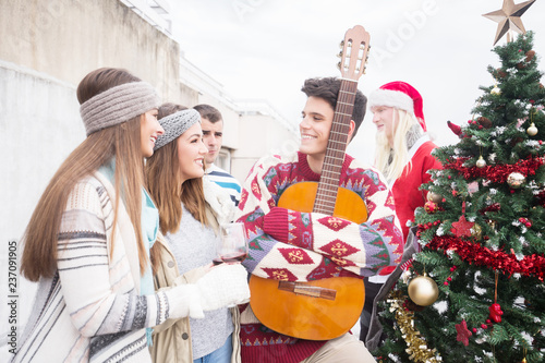 Young man with guitar celebrating Christmas on balcony with friends