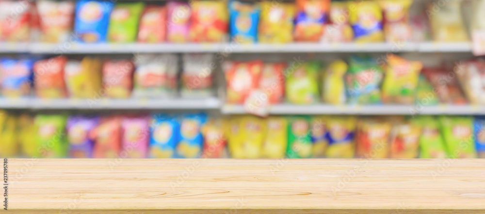 Wood table top with Supermarket convenience store shelves with Potato chips snack blur abstract background