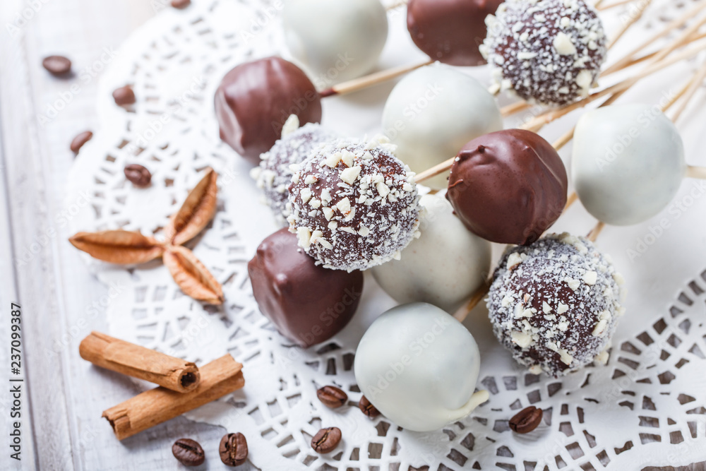 Cake pops decorated with white, dark chocolate and coconut on napkin, natural light selective focus.