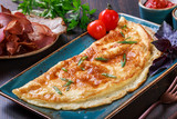 Omelette with prosciutto, slices ham, mushrooms, greens, cheese and tomato sauce on dark wooden background. Hot and healthy breakfast, top view, flat lay