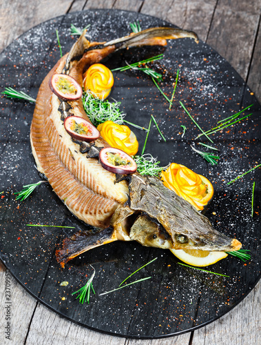 Baked sturgeon fish with rosemary, lemon and passion fruit on plate on wooden background close up. Healthy food. Top view. Russian traditions. Top view photo