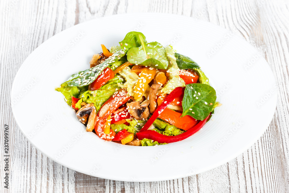 Fresh vegetable salad with lettuce, spinach, grilled mushrooms, tomatoes, sweet peppers and sesame seeds on plate on light wooden background close up. Healthy food. Top view Fresh vegetable salad with lettuce, spinach, grilled mushrooms, tomatoes, sweet peppers and sesame seeds on plate on light wooden background close up. Healthy food. Top view