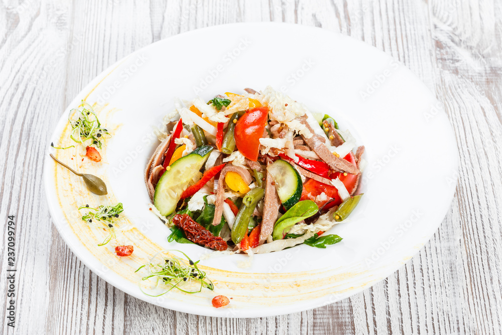 Fresh vegetable salad with cow tongue, spinach, green beans, tomatoes, sweet peppers, cabbage, mustard and dried tomatoes on plate on light wooden background. Healthy food. Top view