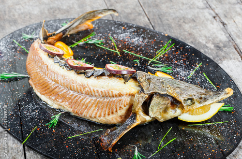 Baked sturgeon fish with rosemary, lemon and passion fruit on plate on wooden background close up. Healthy food. Top view. Russian traditions. Top view photo