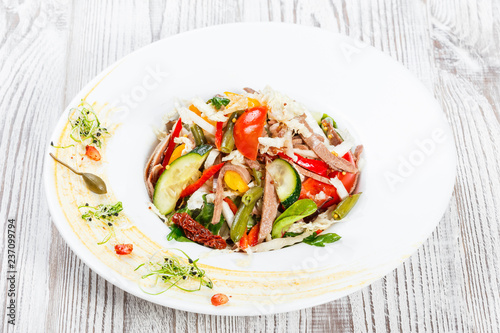 Fresh vegetable salad with cow tongue  spinach  green beans  tomatoes  sweet peppers  cabbage  mustard and dried tomatoes on plate on light wooden background. Healthy food. Top view