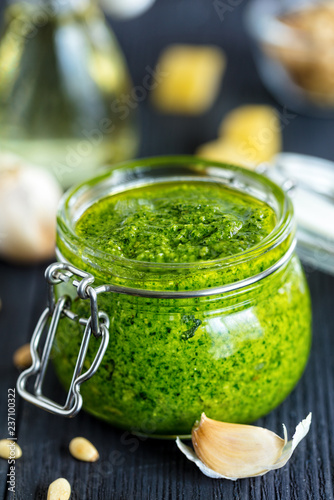 Freshly made Basil pesto sauce in glass jar,  and fresh ingredient on dark background, vertical composition