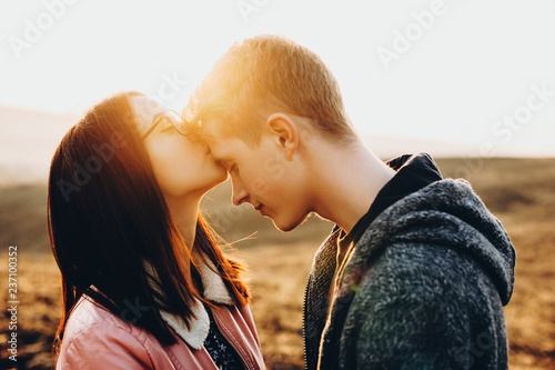 Fotografie Side view of cute young female kissing handsome guy in forehead while standing in field together