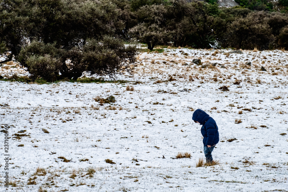 A boy with blue down jacket standing on the ground covered with white snow.