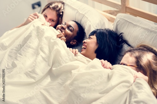 Group of diverse women lying on bed together under the blanket