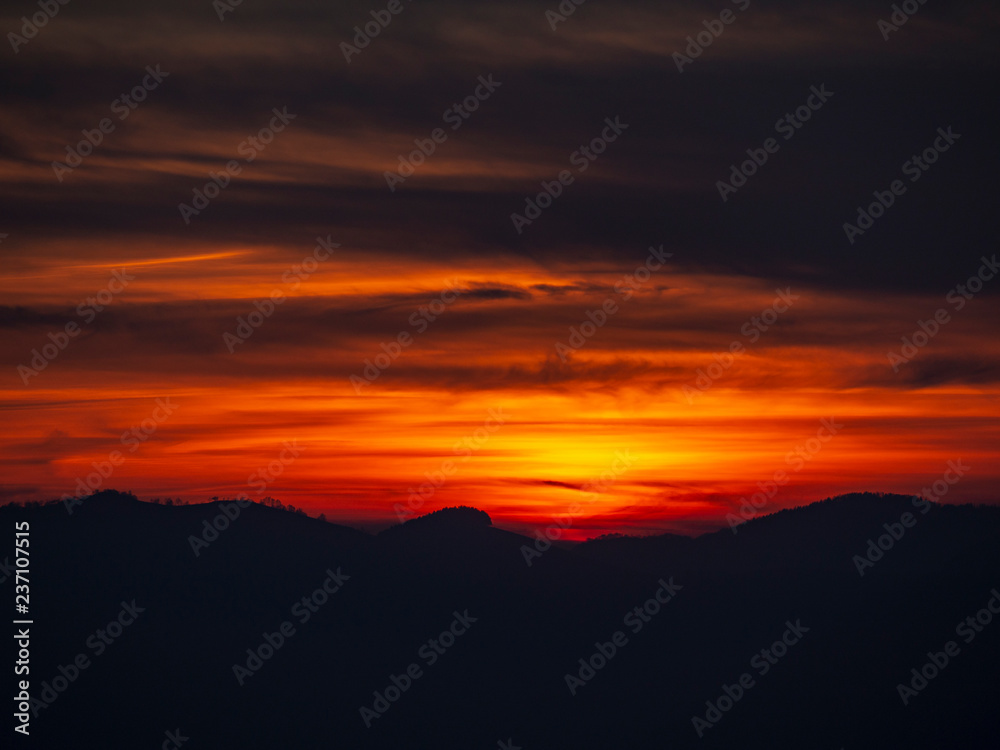 Fiery sunset from mountain peak in a cloudy evening. Fall season. Orobie mountains. Italian Alps