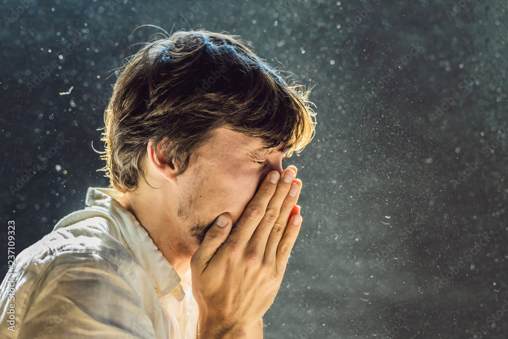 Allergy to dust. A man sneezes because he is allergic to dust. Dust flies in the air backlit by light