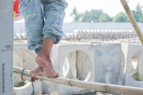 Close up of construction worker's feet treading on a Bamboo Scaffolding, feet with dry heels, cracked skin.