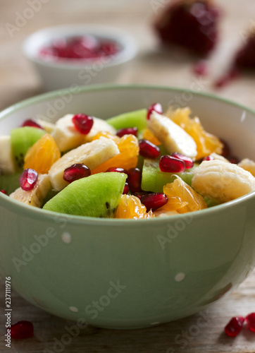 Salad of slices of various fruits and pomegranate seeds on a wooden background.