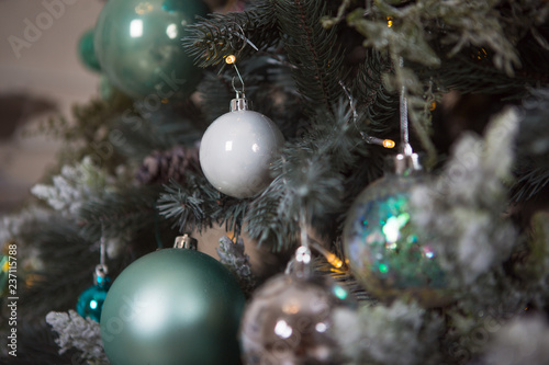 Christmas toys on a green artificial Christmas tree in a gentle style and gold lights garlands. Green, white and blue glass cones and balls decorate the spruce, close-up.