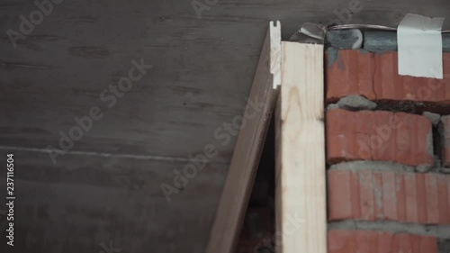 Male worker in white gloves is using new modern mechanical power screw driver to screw yellow wooden planks placed on part of wallr in workerhouse in daylight. photo
