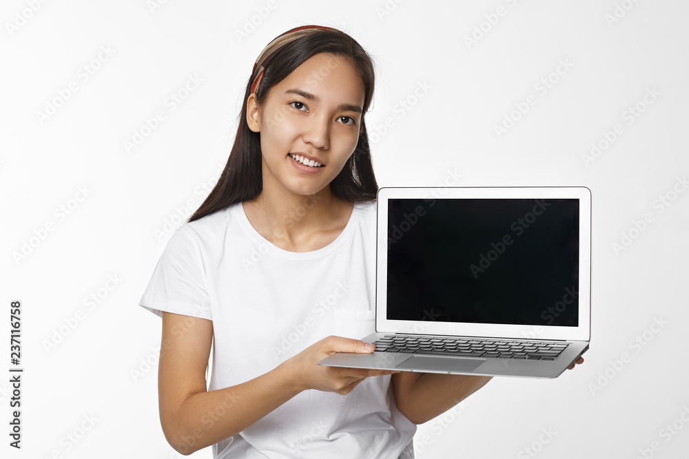Beautiful young brunette Chinese female smiling broadly, holding open laptop pc with black empty display with copy space for your information or advertising content. People and technology concept