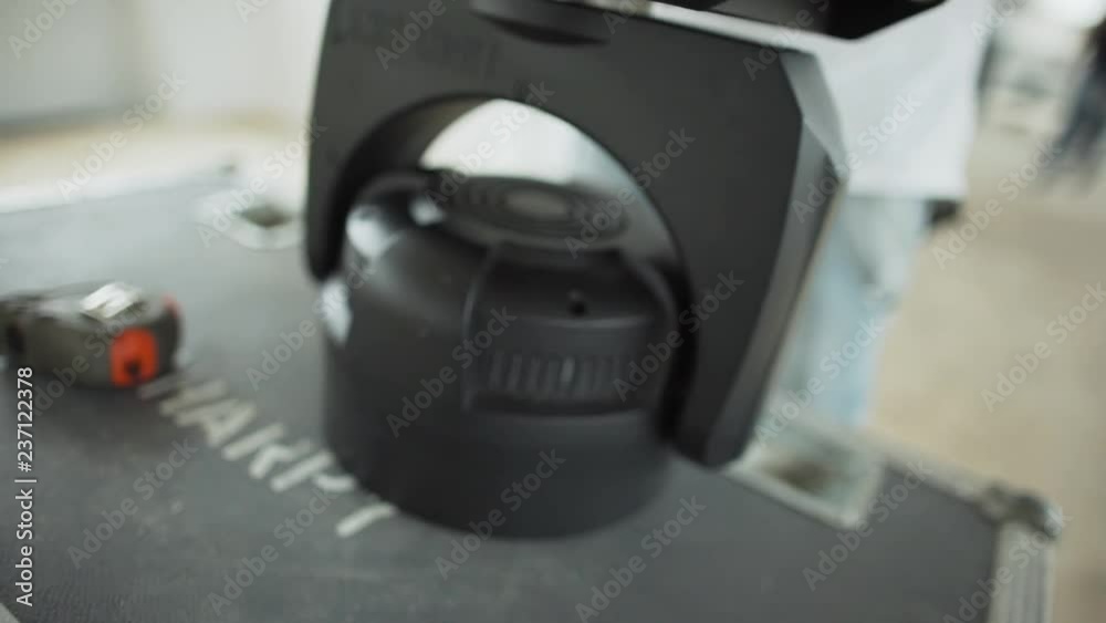 Camera is showing man dressed in white t-shirt is setting and turning different things and handles on black plastic device in daylight room. Camera is showing man dressed in white t-shirt is setting and turning different things and handles on black plastic device in daylight room.