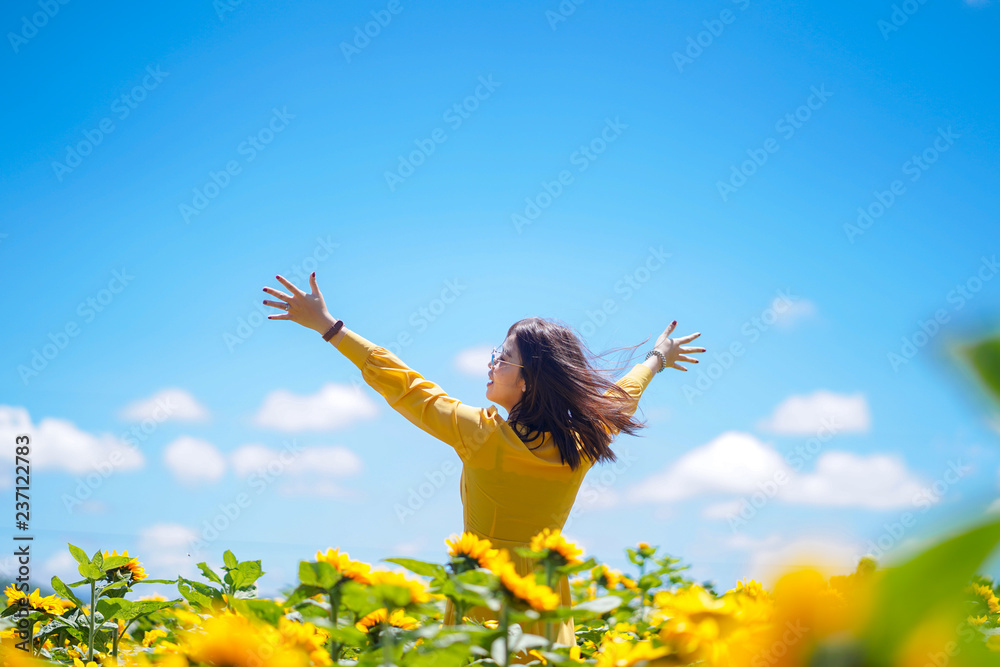 Fototapeta premium Happy carefree summer woman in sunflower field in spring. Cheerful multiracial Asian woman smiling with arms raised up.