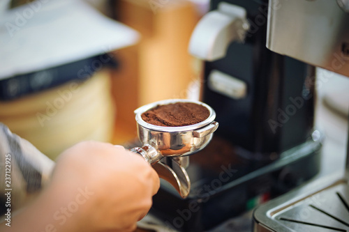 Hand of barista holding portafilter filled with ground coffee preparing to brew with machine. Selective focus.