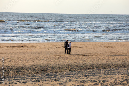 Fototapeta Naklejka Na Ścianę i Meble -  A woman and a man are walking on a sunny day along the beach in Katwijk. Netherlands
