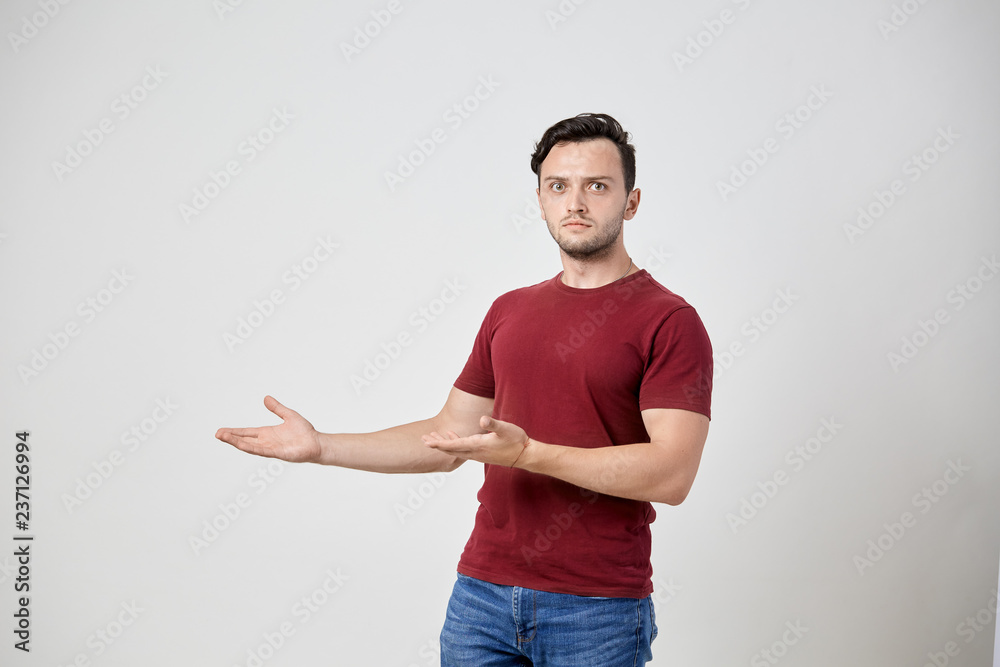 Surprised man in the burgundy t-shirt points to the side with his hands Surprised man in the burgundy t-shirt points to the side with his hands
