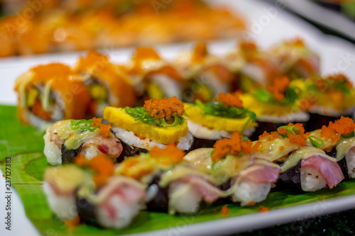 The row of rolled sushi with shrimp orange eggs and sea weed on the white ceramic tray in the incandescent light of restaurant.