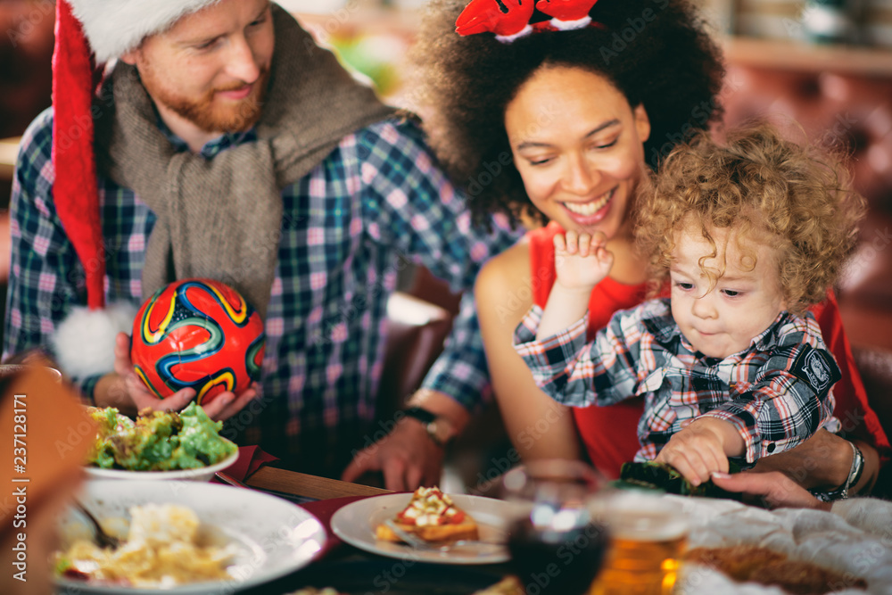 Mixed race woman holding toddler while sitting at table. Christmas eve concept Mixed race woman holding toddler while sitting at table. Christmas eve concept