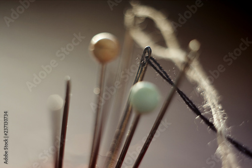 pins with colored knobs, and a needle and thread, sticking out in different directions on the background of dark color