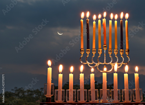 Menorahs with burning candles is traditional symbol for Hebrew Holidays and celebration of Hanukkah. Background of night or dawn sky, selective focus on attributes of Holiday