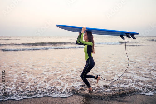 young woman in wet suit holding surfboard over head at beach going to the sea aloha and freedom