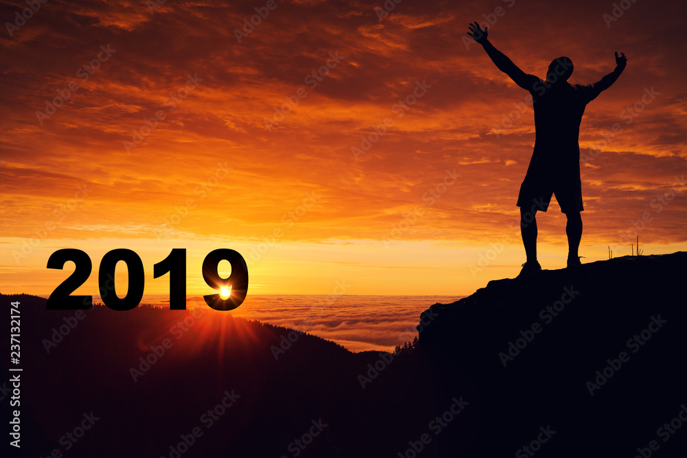 Man silhouette on the mountain top watching the sunrise and 2018 years while celebrating