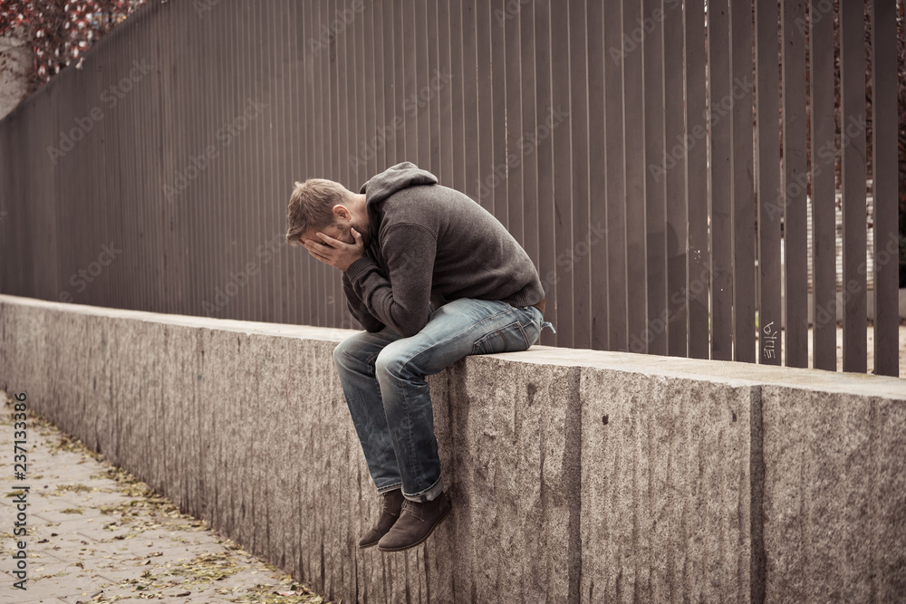 Unhappy depressed caucasian male sitting on urban street feeling Unhappy depressed caucasian male sitting on urban street feeling