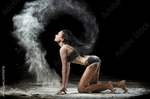 Fototapeta Naklejka Na Ścianę i Meble -  Graceful woman posing in a cloud of dust on a black background