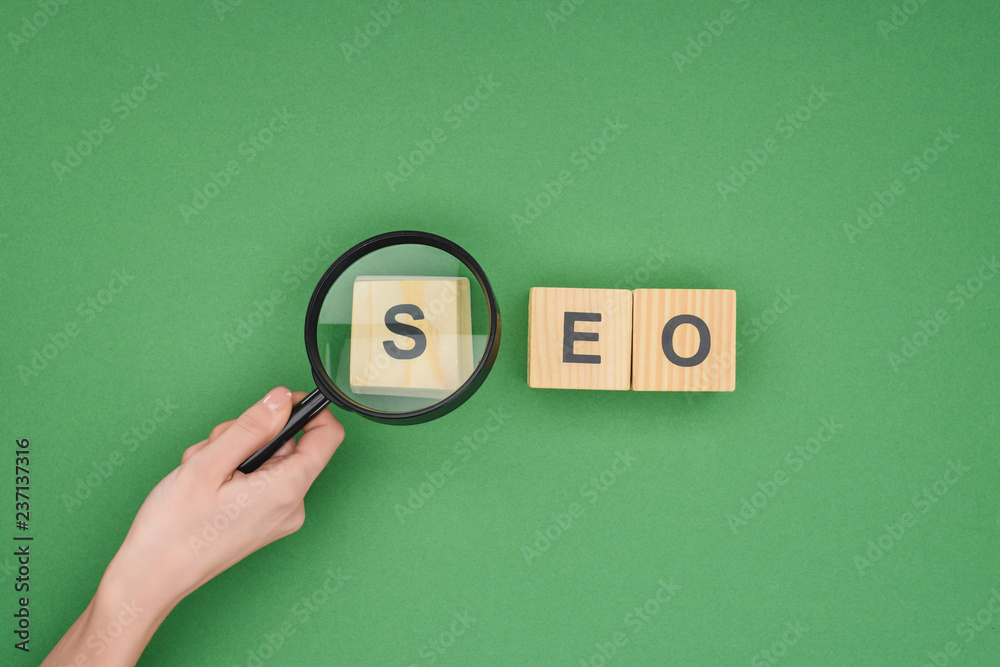Top view of woman holding magnifier over wooden cubes with seo lettering  on green background