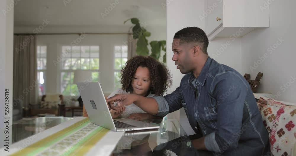 African American father helping daughter with homework using laptop