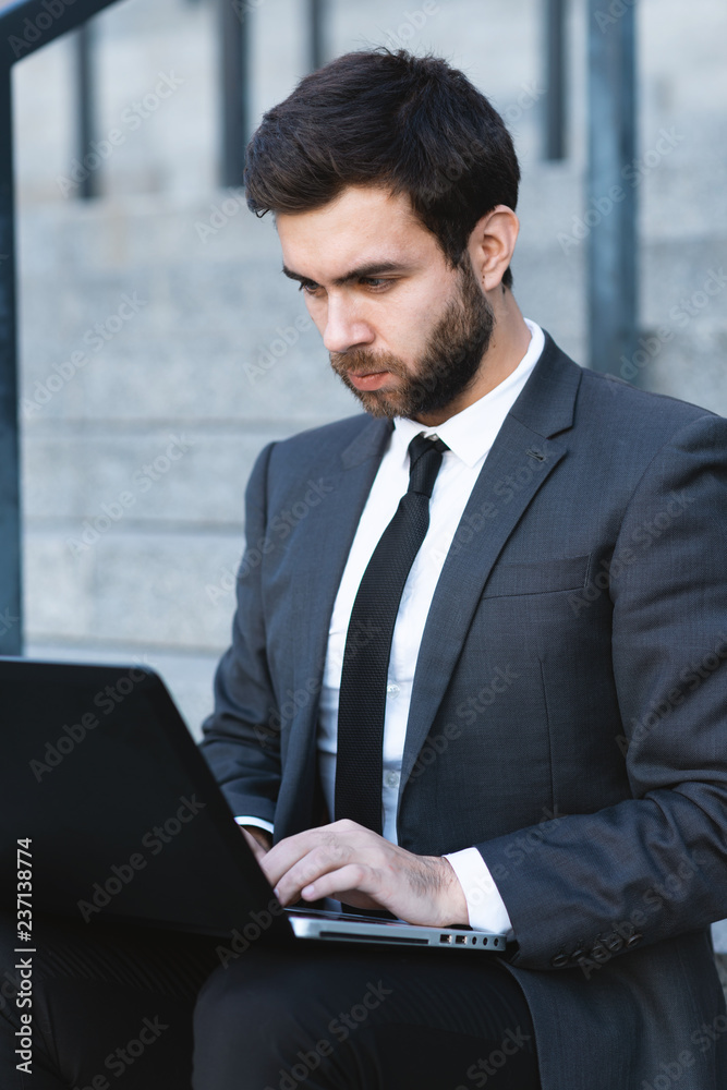 Businessman in a suit sitting on the steps and working on a laptop. Businessman in a suit sitting on the steps and working on a laptop.