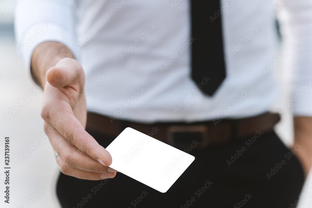 Male hand with white empty business card , close-up photo with selective focus Male hand with white empty business card , close-up photo with selective focus