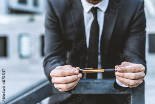 Man in a business suit holds a pen in his hands against the background of an office building. Outdoor