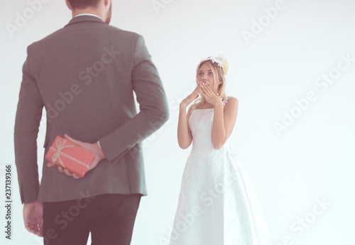 Groom hiding red gift box behind back in order to surprise bride on the wedding day Woman positive emotion and face astonished happy and smling