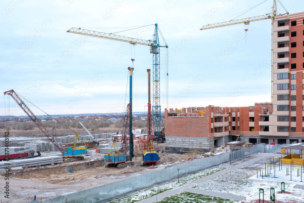 Building with Cranes. Lifting equipment. Crawler cranes, piles, concrete slabs and cranes on the construction site near the multi-storey building. The process of driving piles.