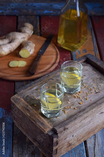 Ginger tincture or ale on wooden background. Spice yellow liqueur in a glass. Homemade Alcohol drink. Rustic style.